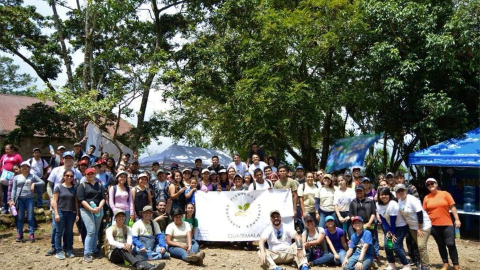 Grupo numeroso de voluntarios reunidos con la bandera de Plantemos al final de una jornada